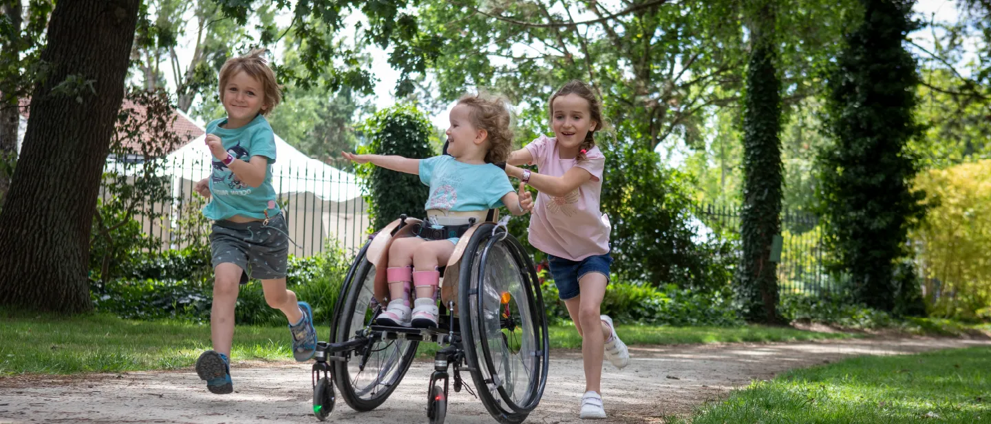 Trois enfants, dont une fillette en fauteuil roulant, jouent et courent ensemble dans un parc arboré — AFM-Téléthon, mobilisation pour les maladies rares