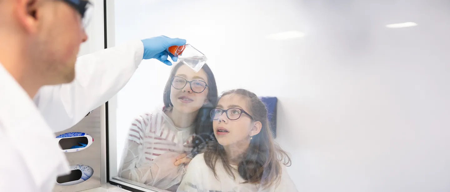 Deux jeunes filles observe une expérience menée par un chercheur à Généthon, un des laboratoires de l'AFM-Téléthon.