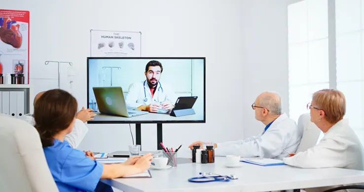 Vignette Actualité - Équipe médicale tenant une conférence en ligne dans la salle de réunion avec un médecin spécialiste de l'homme et prenant des notes sur le presse-papiers. Groupe de médecins discutant du diagnostic sur le traitement des patients par appel vidéo