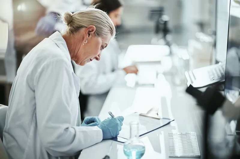 Vignette Actualité : Femme scientifique écrivant sur un porte-bloc dans un laboratoire de recherche médicale