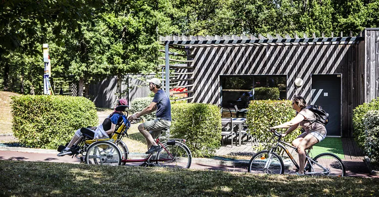 Des vacanciers passent en vélo et en joellette devant une maison en bois à la salamandre