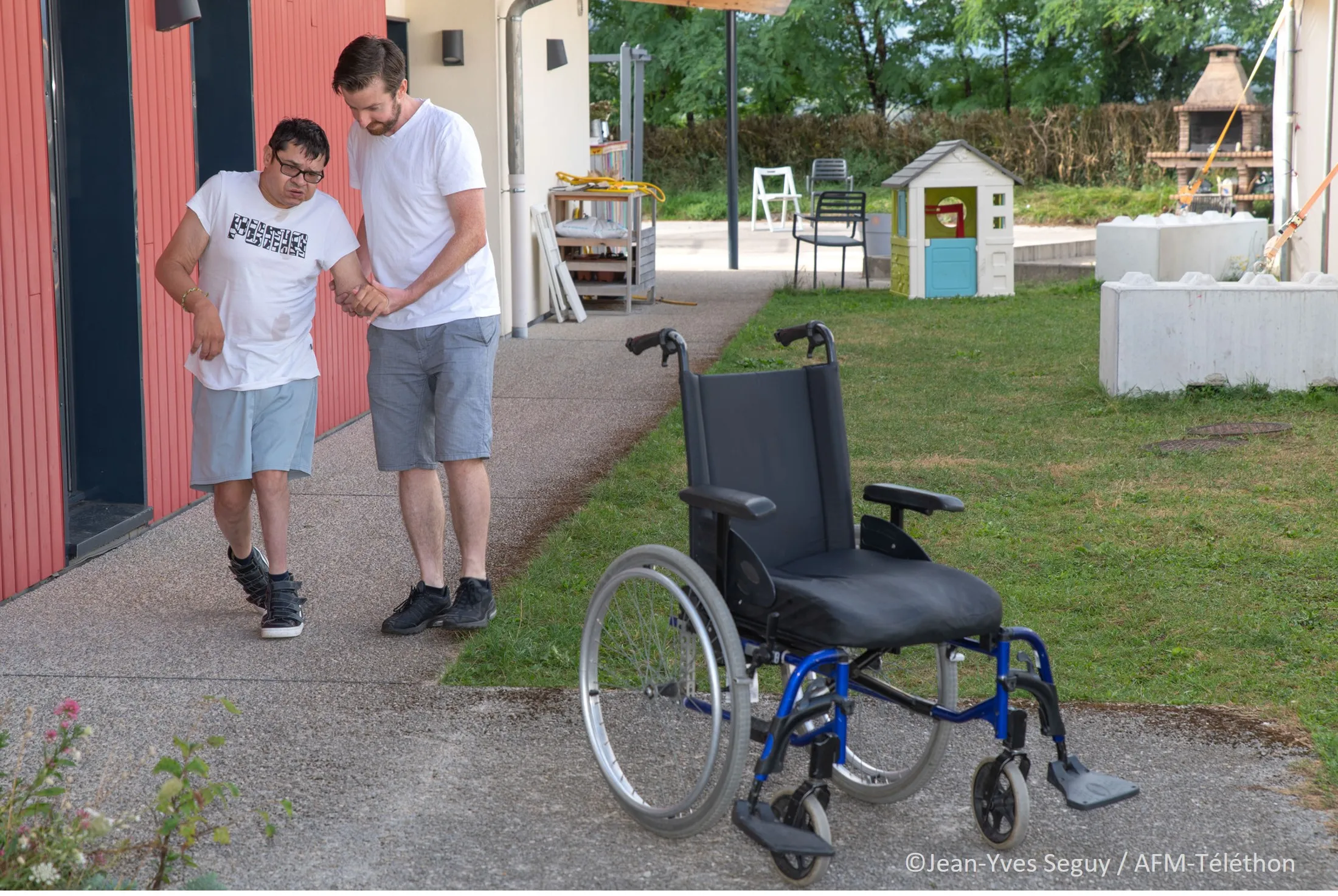 Un kiné aide une personne à s'installer dans son fauteuil roulant