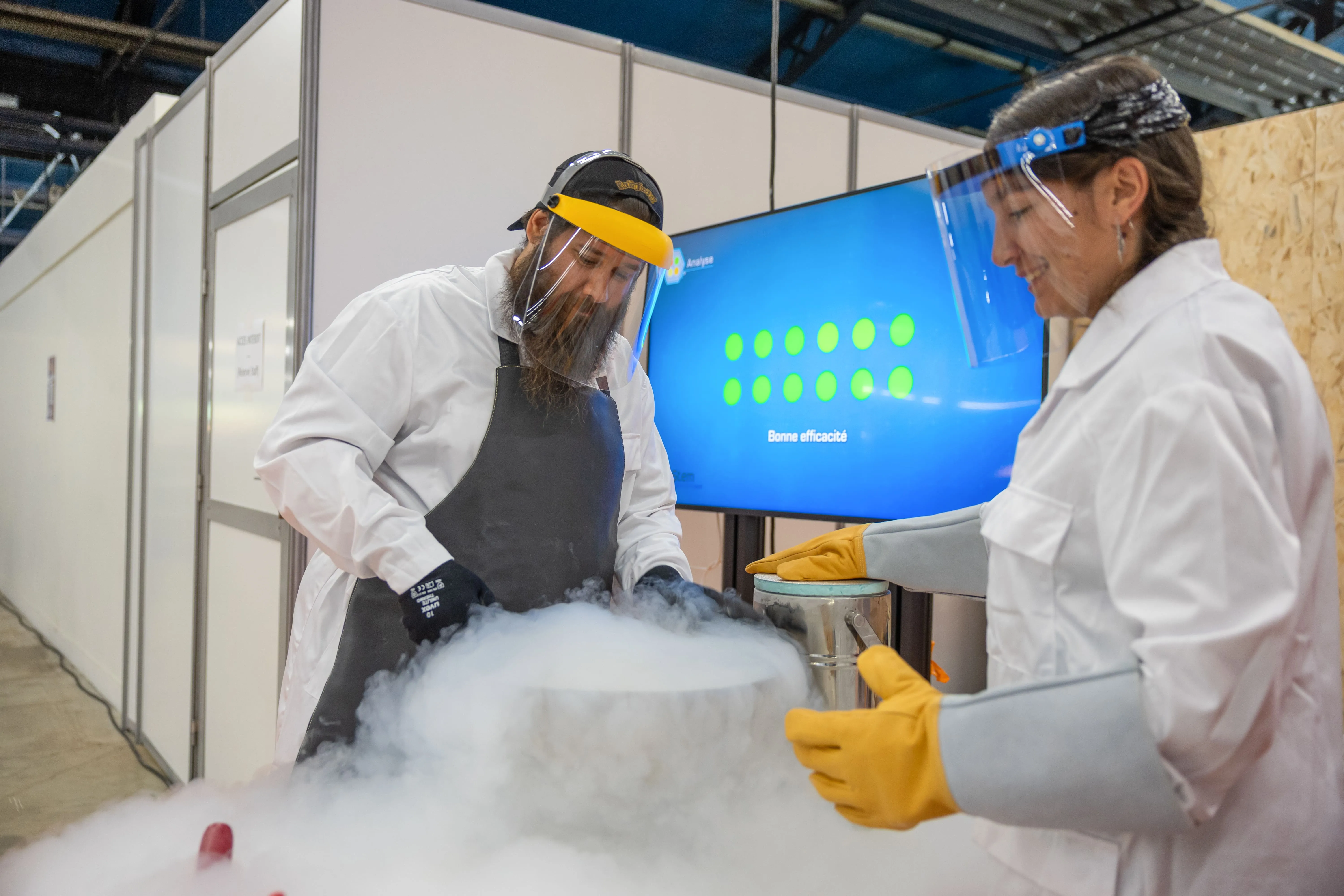 Deux intervenants en blouse blanche et visière de protection manipulent de l’azote liquide lors d’un atelier scientifique, illustrant la rigueur et la pédagogie autour de la recherche.