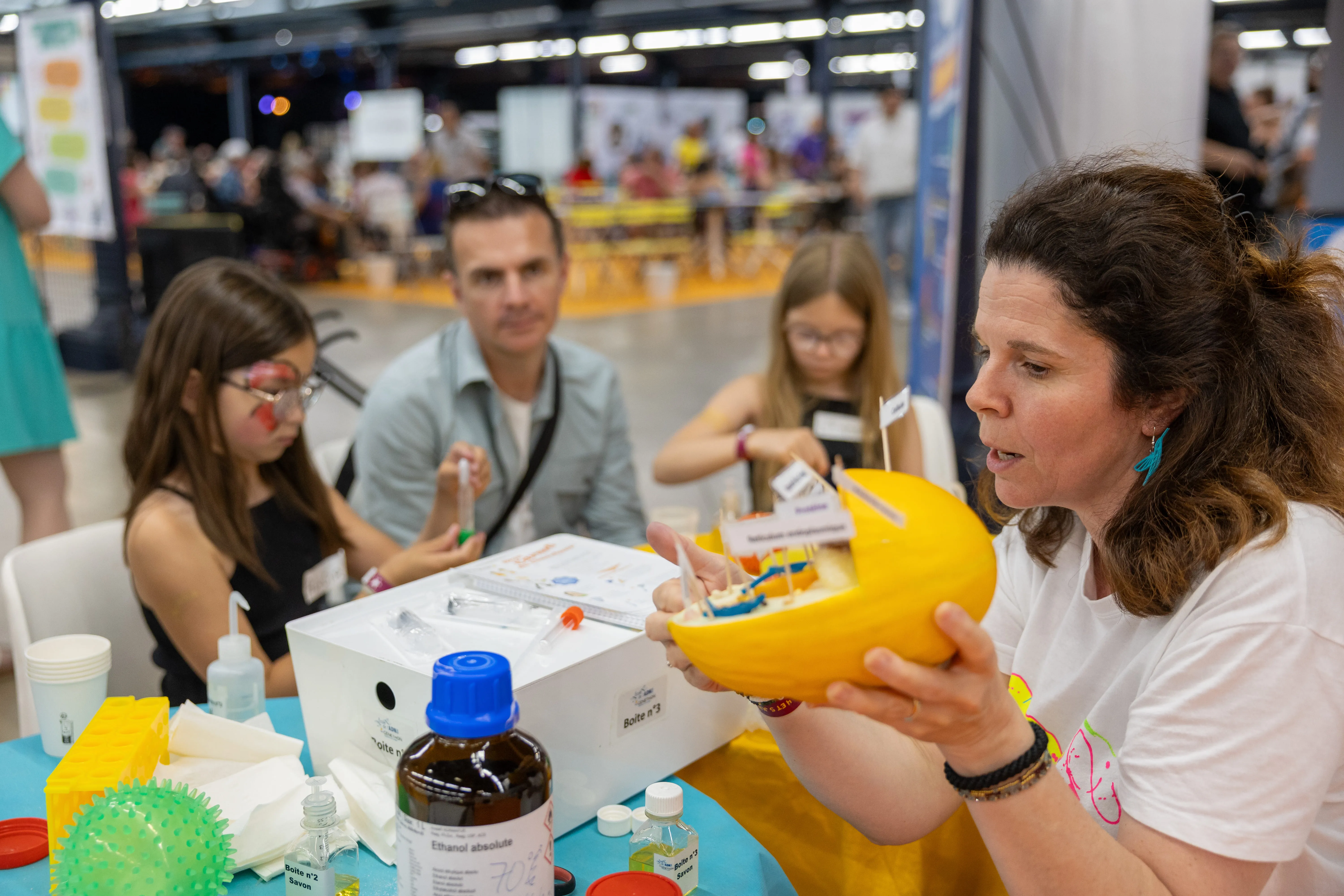 Une médiatrice scientifique explique le fonctionnement d’un organe à l’aide d’une maquette colorée à un groupe d’enfants curieux et concentrés, accompagnés de leurs parents. 