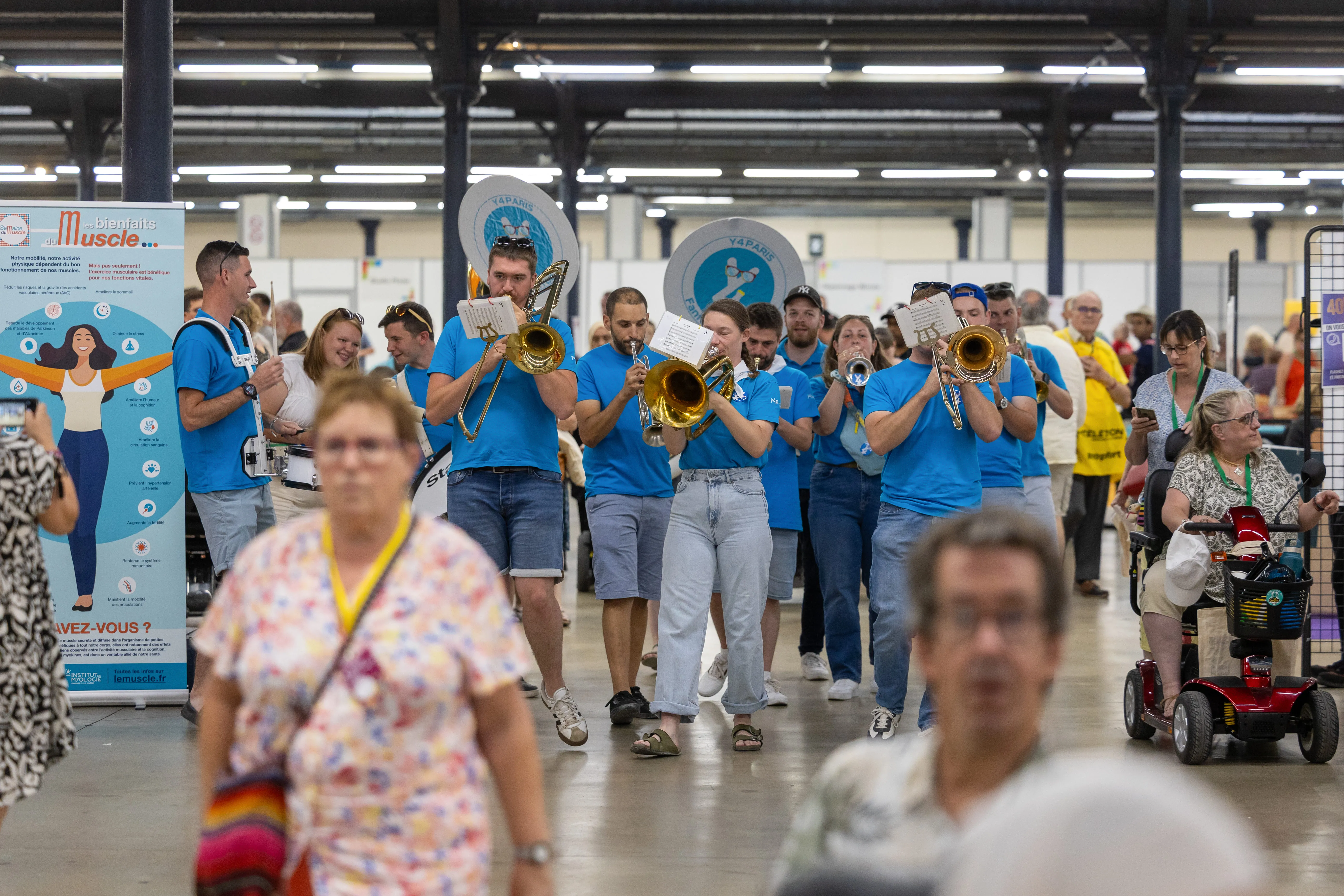 Une fanfare vêtue de t-shirts bleus défile joyeusement dans les allées du salon, apportant une touche festive et musicale aux Journées des Familles.