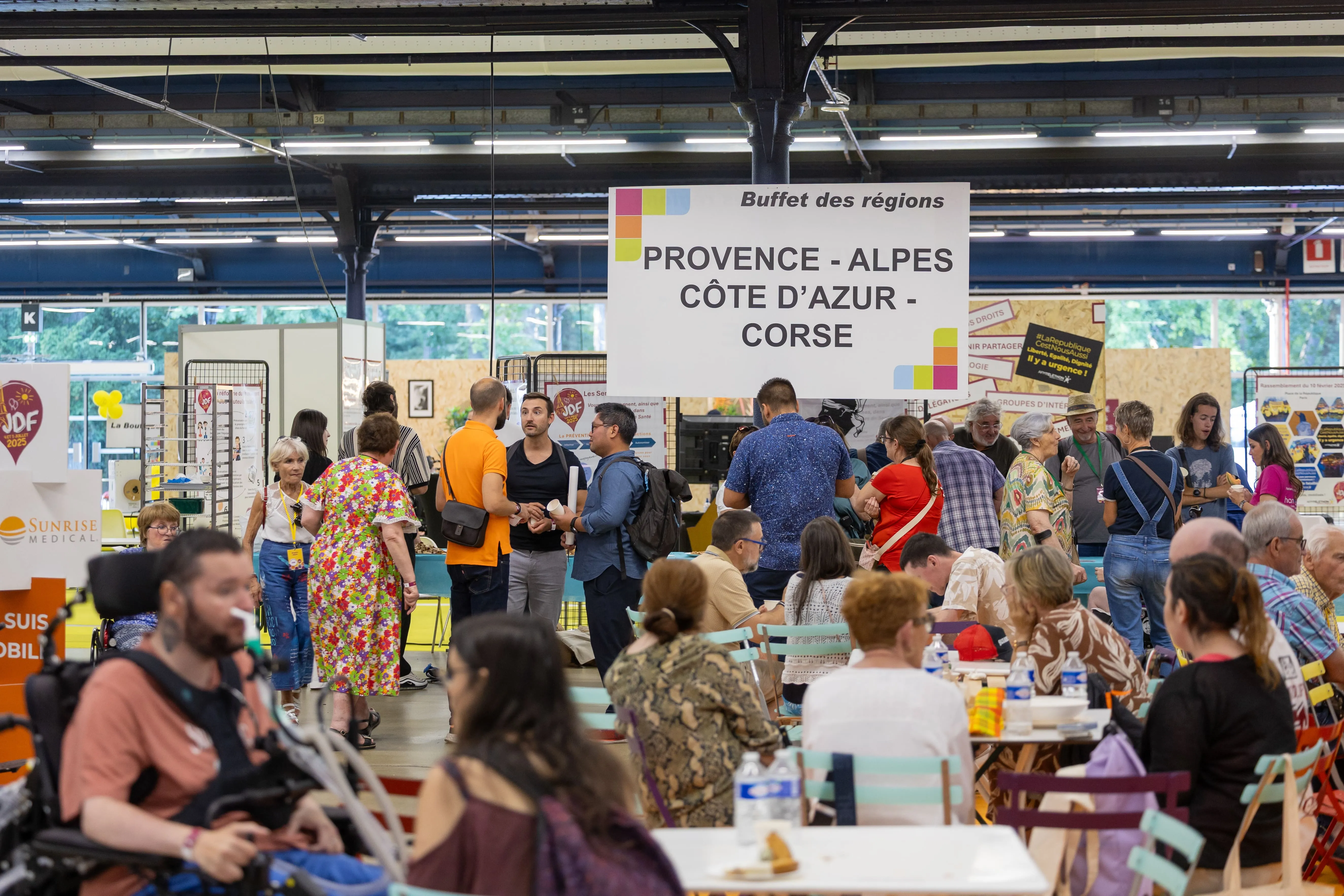 Participants réunis autour du stand ‘Buffet des régions – Provence-Alpes-Côte d’Azur – Corse’, découvrant des spécialités locales dans une ambiance chaleureuse et fédératrice.
