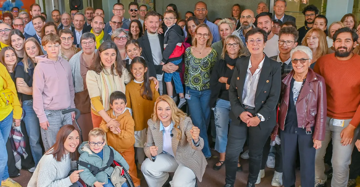 Photo de famille devant l'AFM-Téléthon : salariés, bénévoles, chercheurs et familles ambassadrices réunis autour de Santa et de Laurence Tiennot-Herment.
