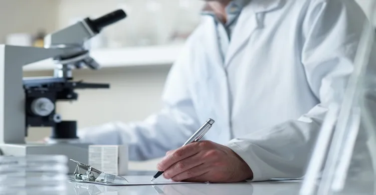 Vignette Actualité - Chercheur dans un laboratoire qui rédige à côté d'un microscope