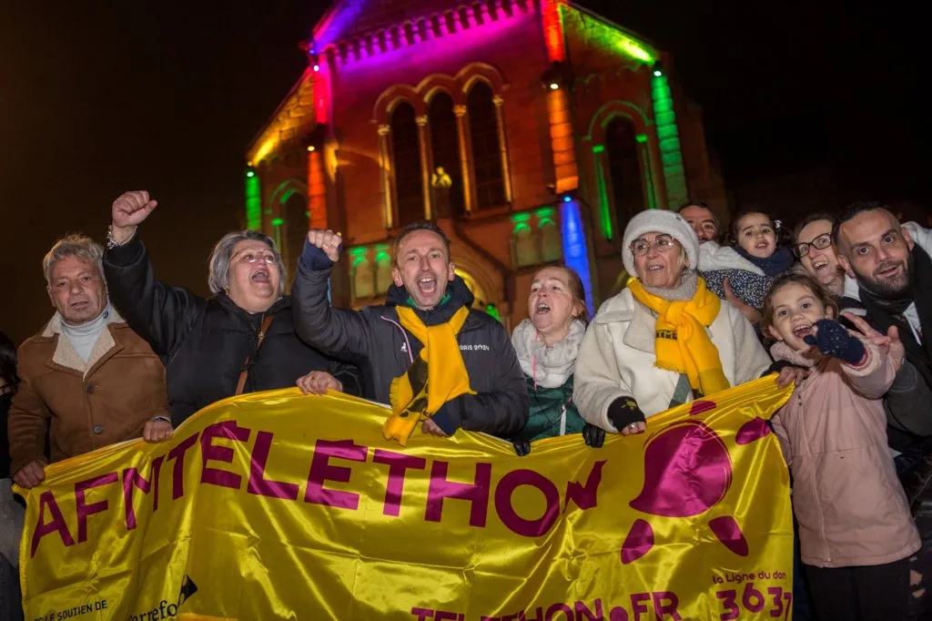 La solidarité en lumière à Firminy : habitants et bénévoles affichent leur enthousiasme devant une église illuminée aux couleurs du Téléthon