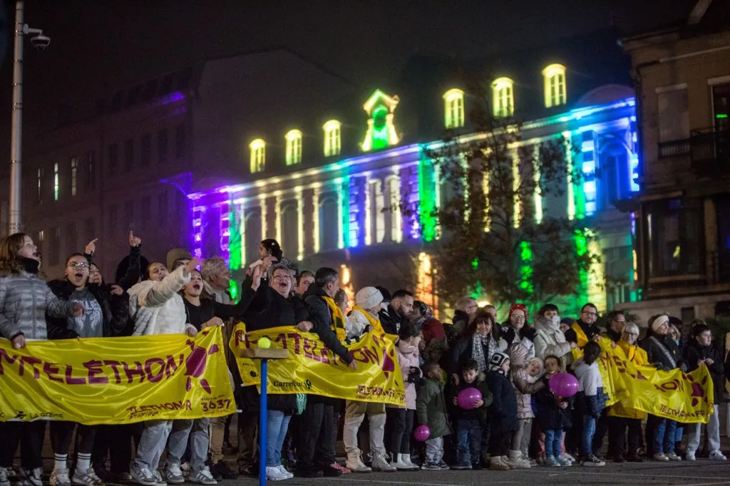 Firminy illuminée pour le Téléthon : une foule enthousiaste se rassemble avec des banderoles et des sourires pour soutenir la recherche.