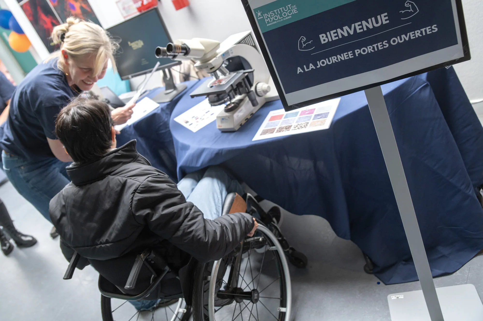 Une chercheuse de l’Institut de Myologie échange avec un visiteur en situation de handicap, devant un poste de microscopie optique, pour mieux comprendre la structure du tissu musculaire.