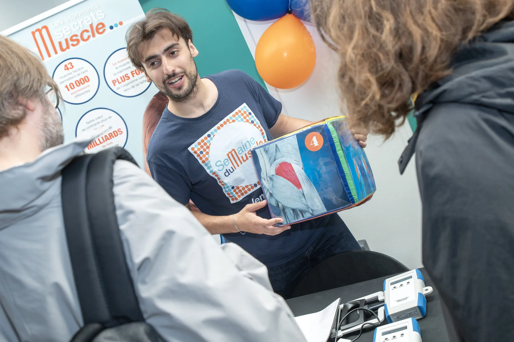 Un animateur présente le cube pédagogique illustrant la répartition des muscles dans le corps humain, dans un stand dédié à la vulgarisation scientifique.