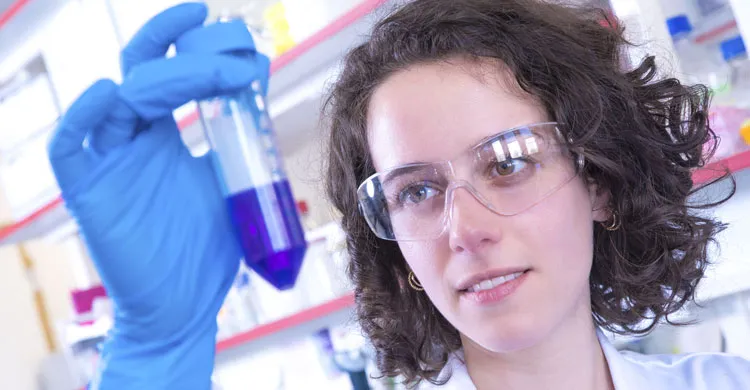 Chercheuse observant un tube dans lequel figure un liquide bleu