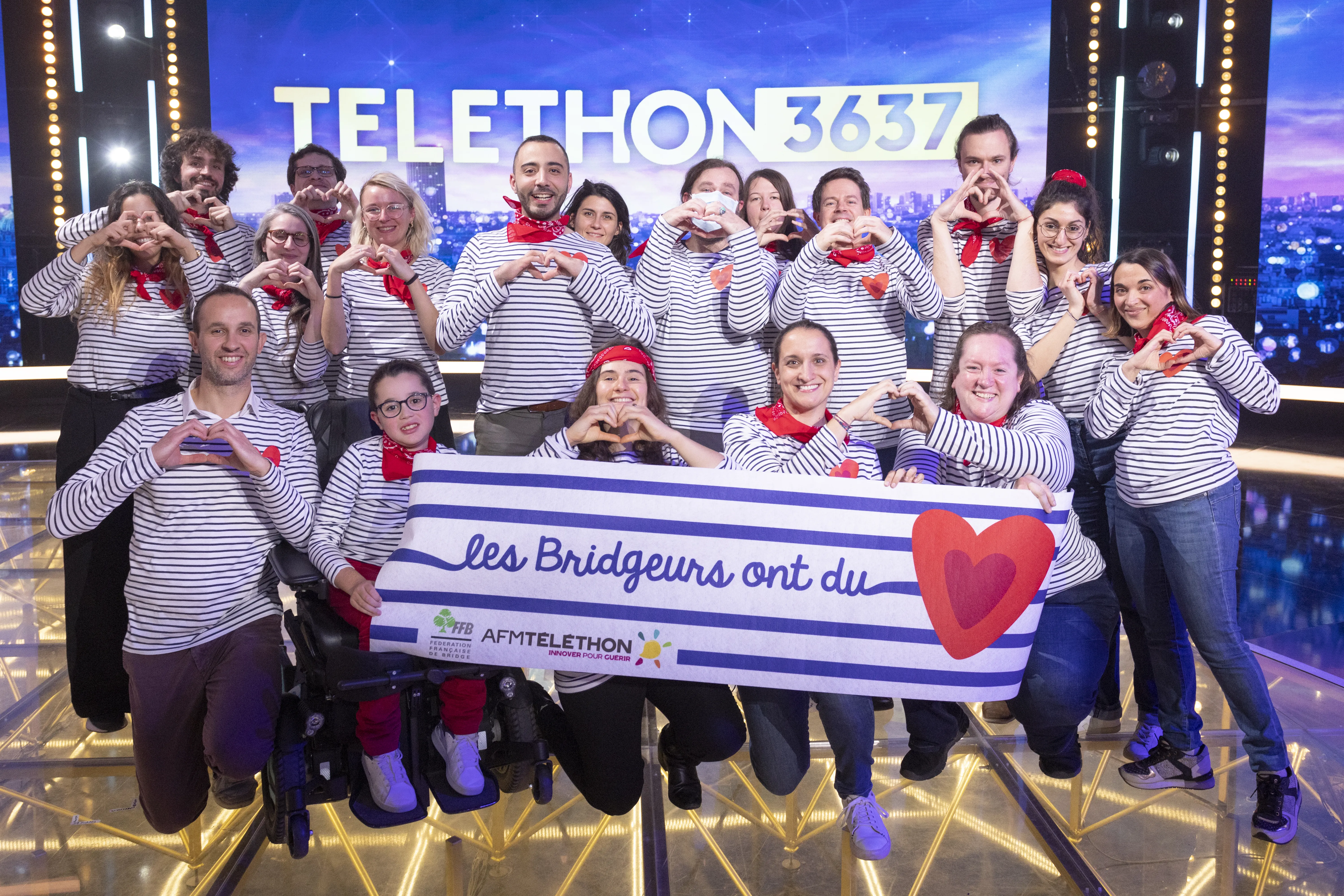 les membres de la fédération française de bridge font un coeur avec les doigts sur le plateau du téléthon