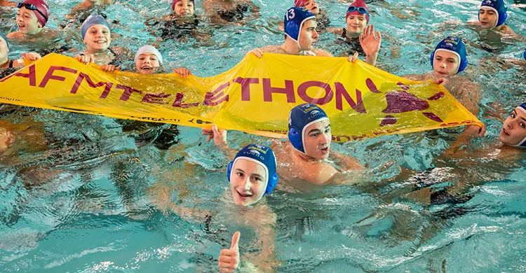 Des bénévoles tiennent une banderole téléthon dans la piscine